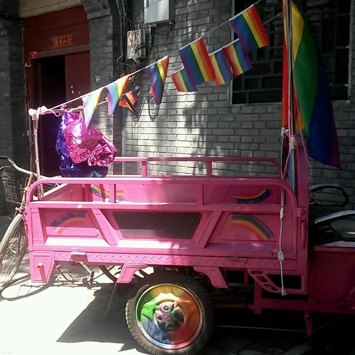 A bright pink sanlunche draped with Pride flags in a Beijing hutong, 2016.