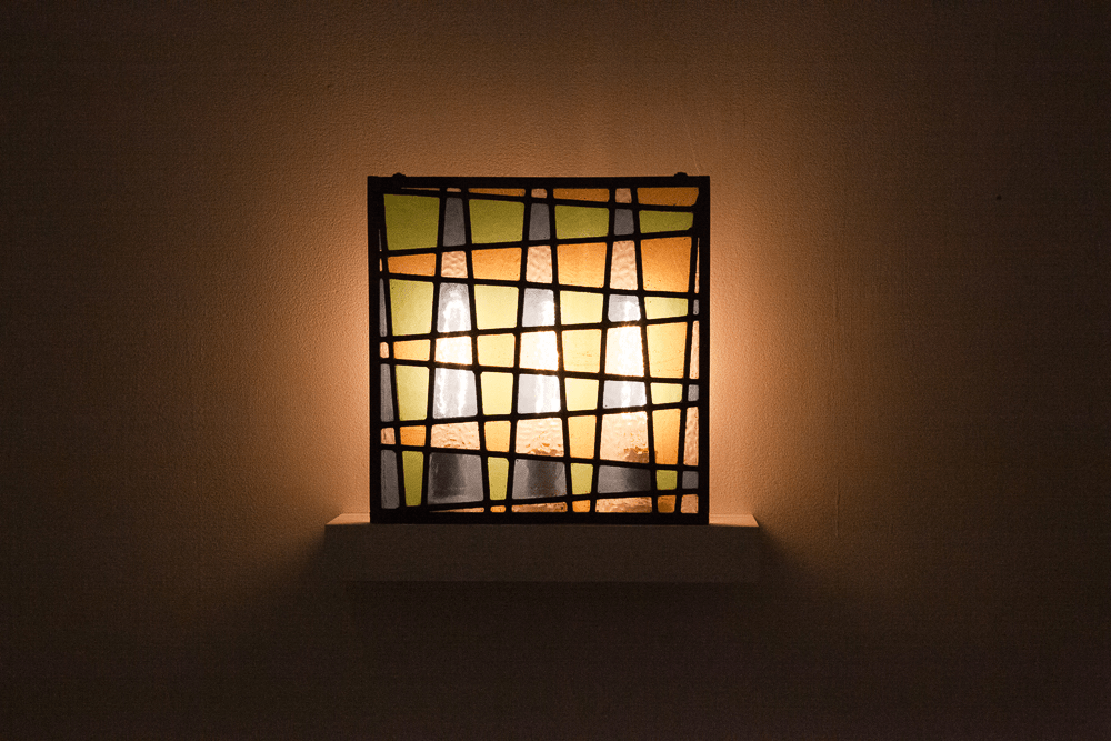 Image of a backlit stained glass panel in yellow, blue, green and clear glass. 